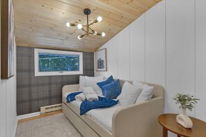 Quarto com cama, janela com vista, luminária no teto e uma pequena mesa com uma planta.