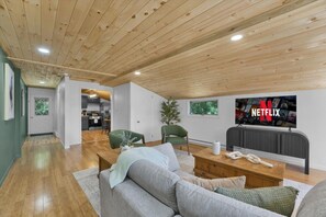Una sala de estar moderna con un sofá gris, una mesa de centro de madera y un televisor que muestra el logotipo de Netflix.