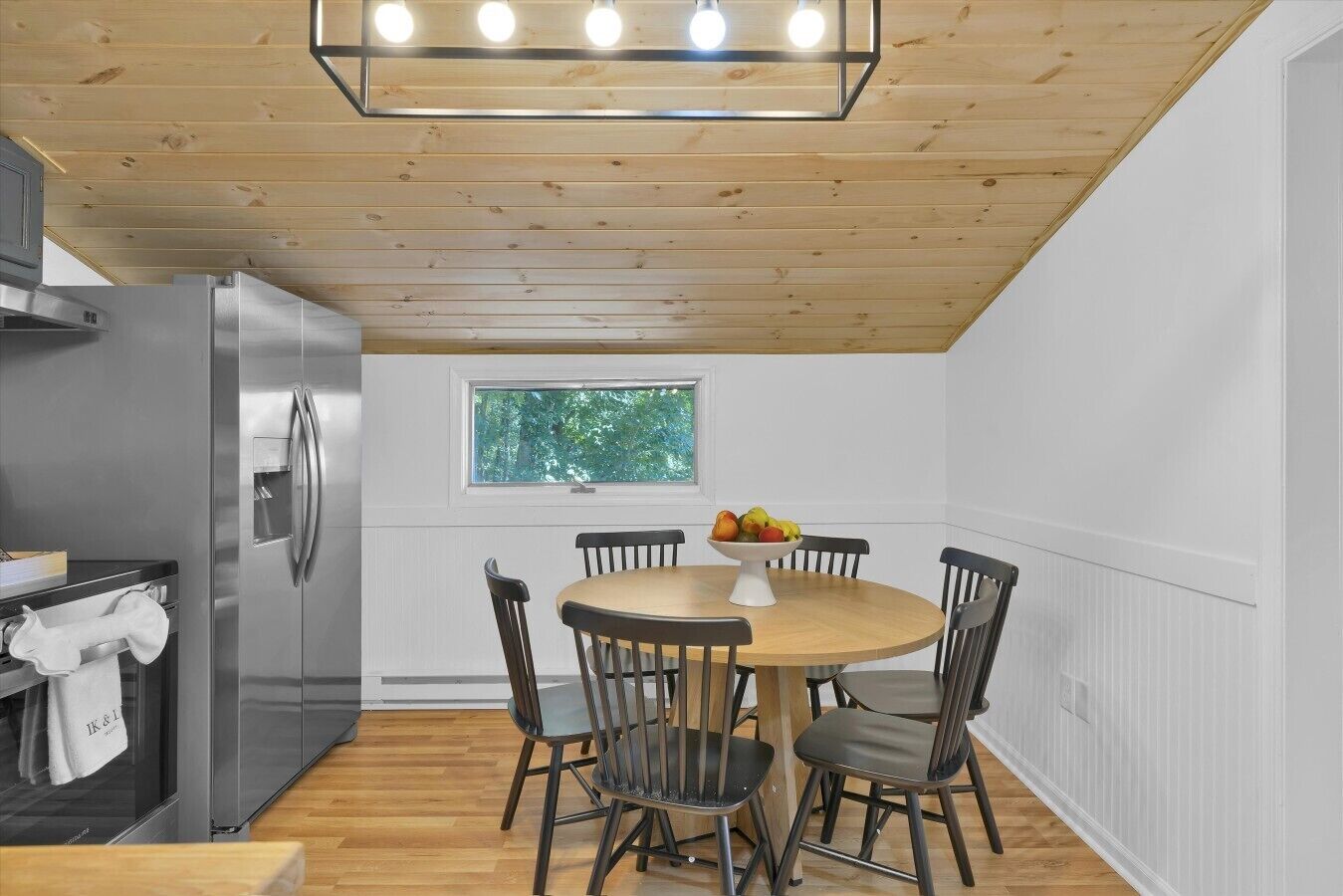 A modern kitchen with a stainless steel refrigerator, a wooden ceiling, and a round dining table with chairs.