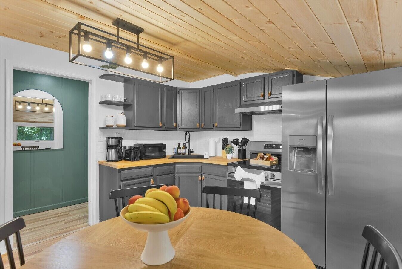 Una cucina moderna con mobili grigi, un frigorifero in acciaio inossidabile e un tavolo da pranzo in legno con una ciotola di frutta.