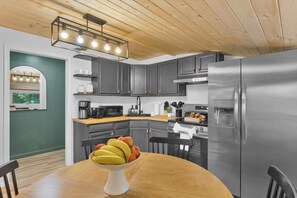 Una cocina moderna con gabinetes grises, un refrigerador de acero inoxidable y una mesa de comedor de madera con un frutero.