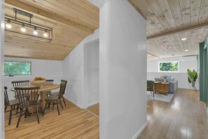 Un interior moderno con comedor que incluye una mesa redonda y sillas, sala de estar con sofá y una mesa de centro, y techo de madera.
