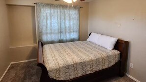 A bedroom with a bed, a ceiling fan, a window with curtains, and a carpeted floor. - Legacy Sports Arizona Family Vacation (San Tan Valley)