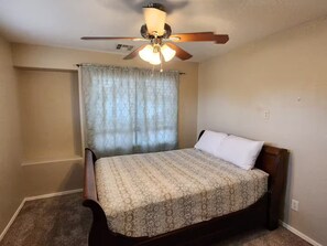 A bedroom with a bed, a ceiling fan, a window with curtains, and a carpeted floor. - Legacy Sports Arizona Family Vacation (San Tan Valley)