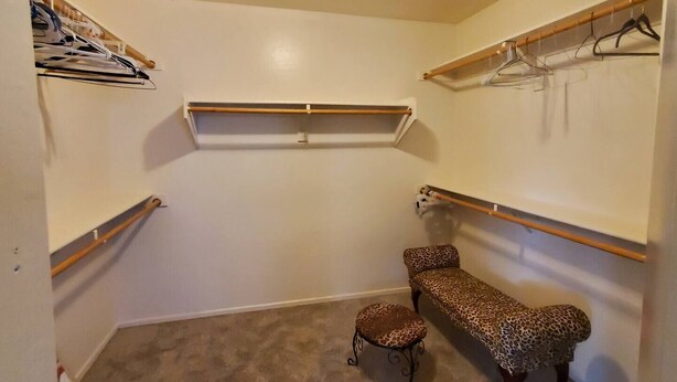 A walk-in closet with built-in shelves for hanging clothes, a bench, and a small stool. - Legacy Sports Arizona Family Vacation (San Tan Valley)