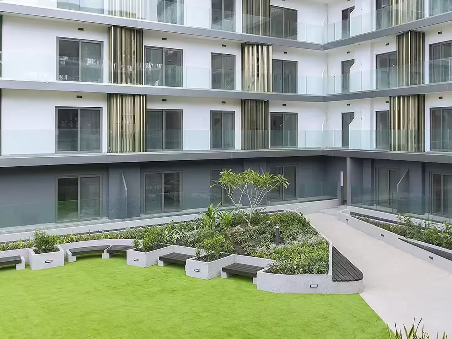 A multi-level residential building with balconies, a central courtyard with grass and plants, and a modern architectural design.
