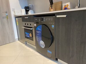 Eine kompakte Küche mit integriertem Geschirrspüler, Backofen und Kaffeemaschine auf der Arbeitsfläche.