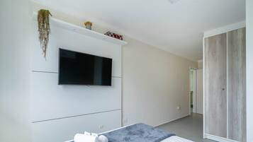 A modern bedroom with a bed, a flat-screen TV mounted on the wall, a wardrobe, and a hanging plant.