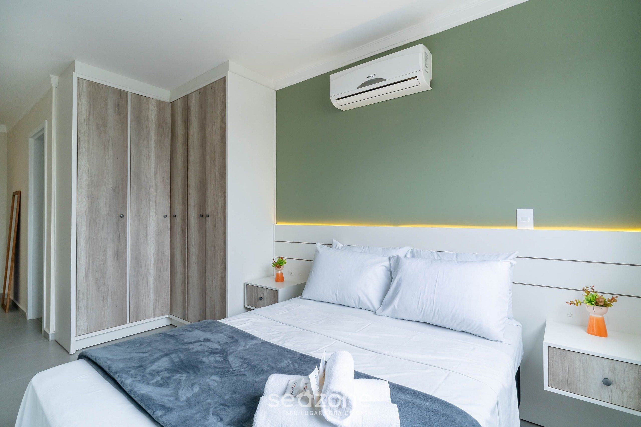 A modern hotel room with a bed, a nightstand, a wardrobe, and an air conditioning unit.