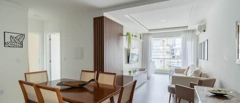 Una sala de estar moderna con comedor, televisor montado en la pared y vistas a la ciudad a través de amplios ventanales.