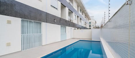 A swimming pool with tiled walls, a tiled deck, and a metal ladder.