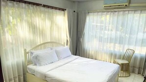 Ein Schlafzimmer mit Bett, Vorhängen, einem Sessel und einer Klimaanlage.