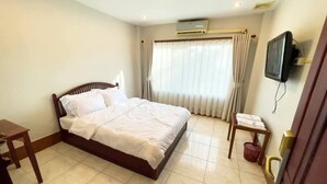 Ein Hotelzimmer mit einem Bett, einem Schreibtisch, einem Sessel, einem Fernseher und einer Klimaanlage.