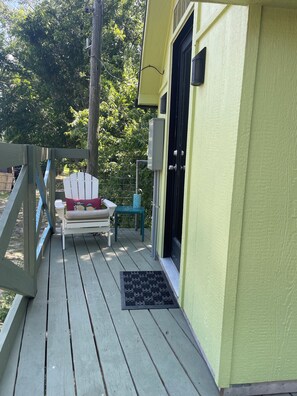 A wooden deck with a white chair and a small table, a door, and a green wall.
