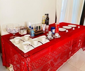 Mesa posta com xícaras, pires brancos e toalha de mesa vermelha.