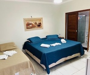 Habitación de hotel con cama, una mesita, una silla, un cuadro en la pared y una puerta que da al baño.