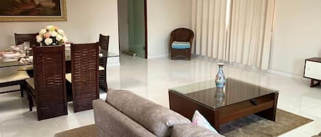 A modern living room with a glass dining table, a sofa, a coffee table, and a chair.