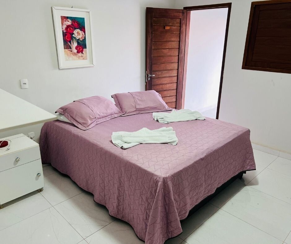 A bedroom with a bed, a nightstand, a door, and a wall-mounted picture.
