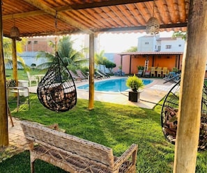 Un espacio al aire libre cubierto con piscina, muebles de mimbre y sillas colgantes.