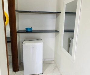 Uma cozinha compacta com geladeira branca, cesta azul e duas prateleiras pretas.