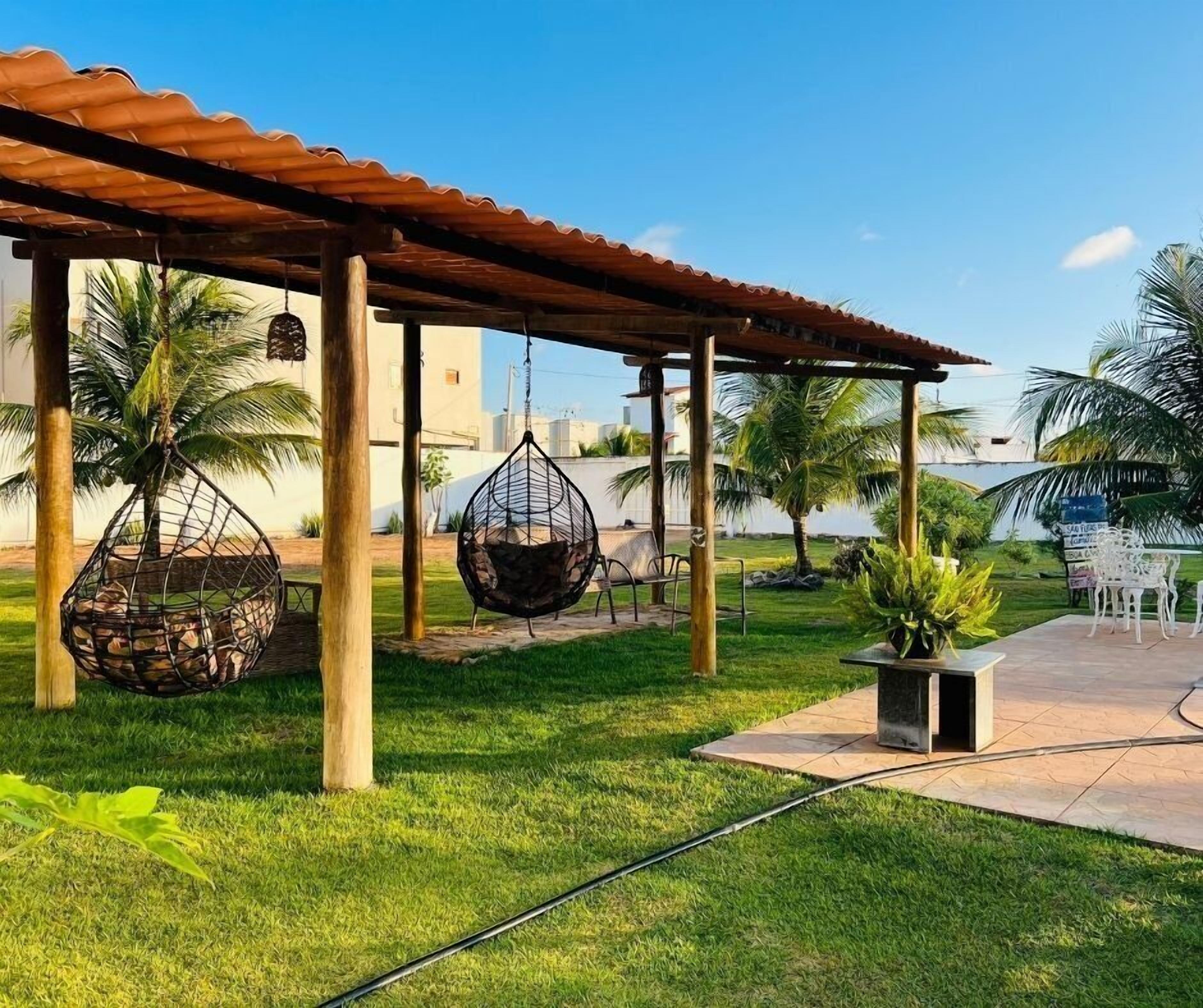 A covered outdoor seating area with hanging chairs, palm trees, and a view of the ocean.