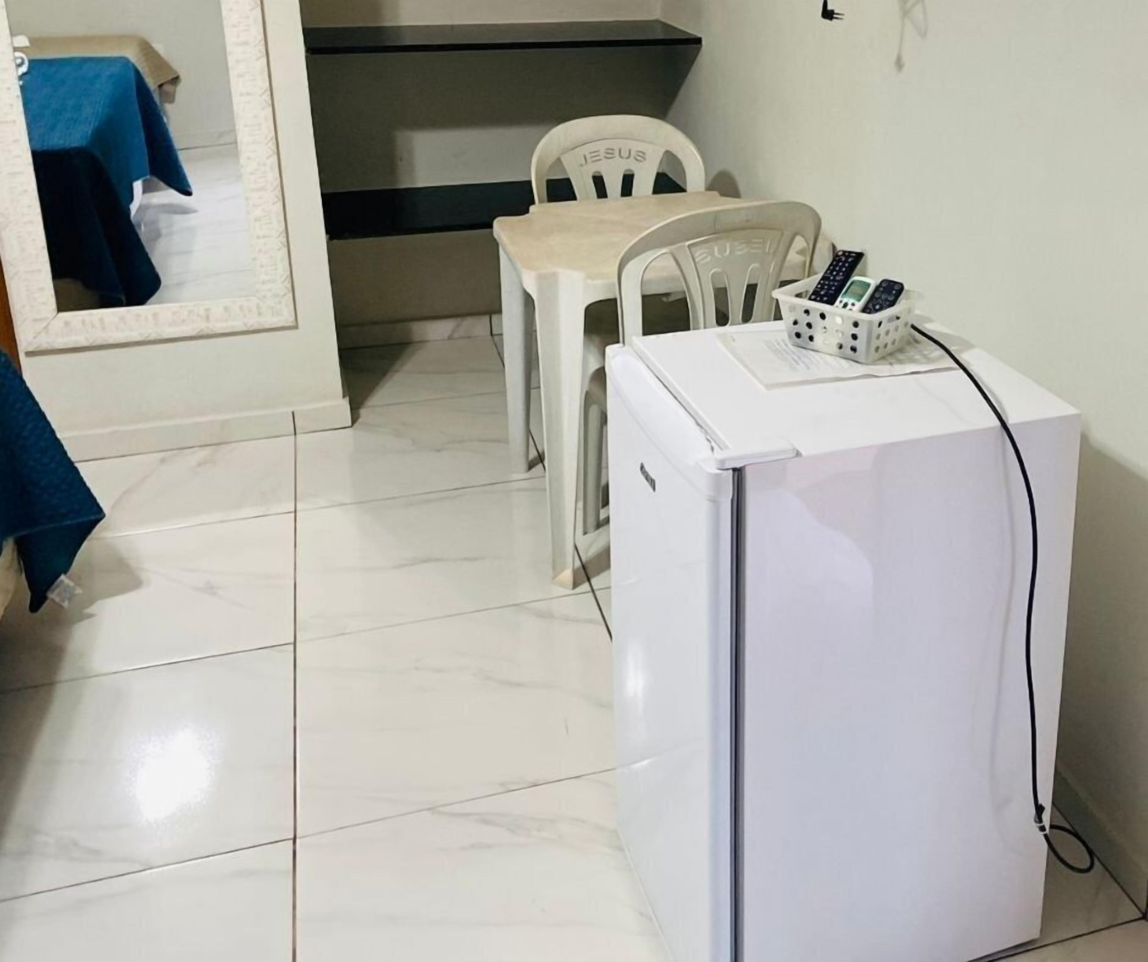 Uma cozinha compacta com geladeira branca, uma mesa de jantar com duas cadeiras e um espelho com moldura decorativa.