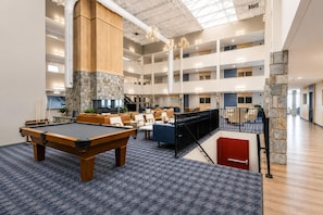 Un espace intérieur à plusieurs niveaux comprenant une table de billard, des coins salon et un mur décoratif en pierre.