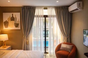 A hotel room with a bed, a chair, a lamp, a painting, and a window with curtains. - Urban Studio+BigComfy Bed+EmbsyGdns, Cantonments (Accra)