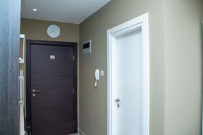 A hallway with a dark wooden door, a white door, a clock, and a phone on the wall. - Urban Studio+BigComfy Bed+EmbsyGdns, Cantonments (Accra)