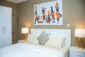 Ein Hotelzimmer mit einem Bett, zwei Nachttischlampen, einem großen abstrakten Gemälde an der Wand und einem Kleiderschrank.