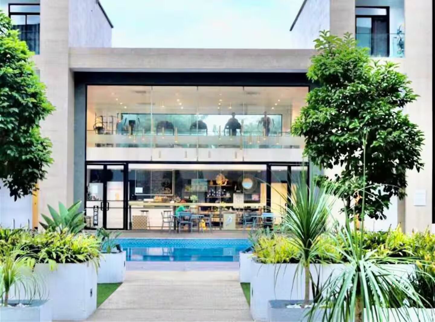 A modern building with a glass facade, a pool, and potted plants.