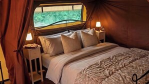 A tent with a bed, two bedside lamps, and a window. - The Safari Tent at Pencwm Escapes (Hebron)