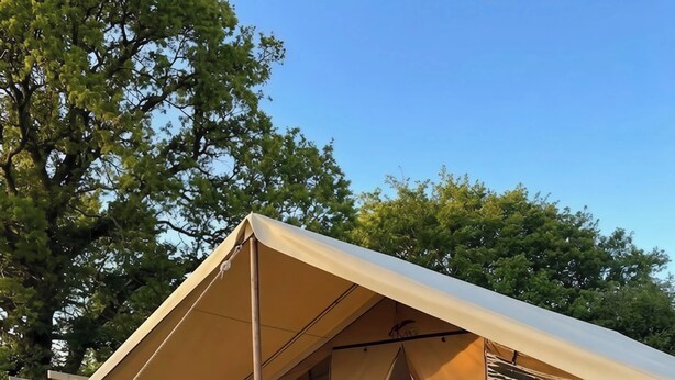 A tent with a wooden deck, a bed, a chair, and a table. - The Safari Tent at Pencwm Escapes (Hebron)