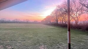 Ein Außenbereich mit einer Rasenfläche, einer Holzterrasse und einem Gebäude mit Dach.