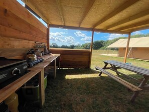 A rustic wooden cabin with a kitchen area, a dining table, and a picnic bench. - The Safari Tent at Pencwm Escapes (Hebron)