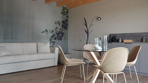 A modern living room with a sofa, dining table, chairs, and a kitchen area with appliances. - Dominò Apartment with a Stunning View of the Euganean Hills (Veneto)