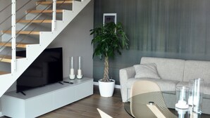 A modern living space with a wooden staircase, a grey sofa, a coffee table, and a potted plant. - Dominò Apartment with a Stunning View of the Euganean Hills (Veneto)