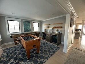 A room with a foosball table, a refrigerator, and a kitchen area with shelves. - Spacious 5-Bedroom house on the bay with large dock and open water, sunset views (Brigantine)
