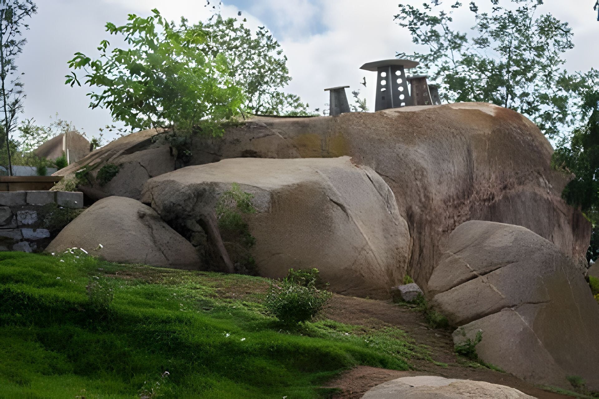 A rock formation with a small waterfall, surrounded by grass and trees.