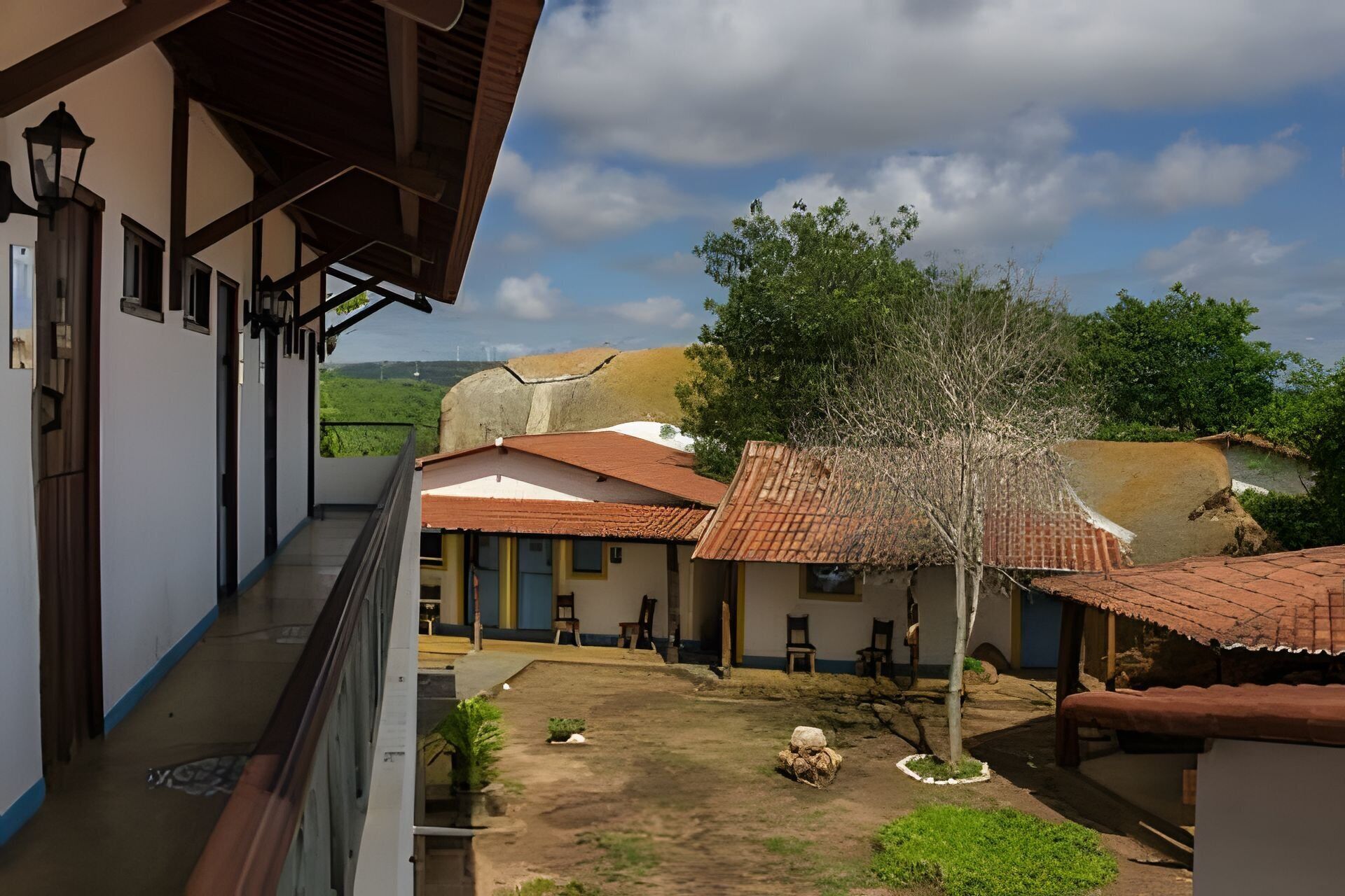 A courtyard with buildings, a tree, and a view of the landscape.