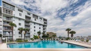 Ein Hotelpoolbereich mit blauem Himmel, einem mehrstöckigen Gebäude mit Balkonen und Palmen.