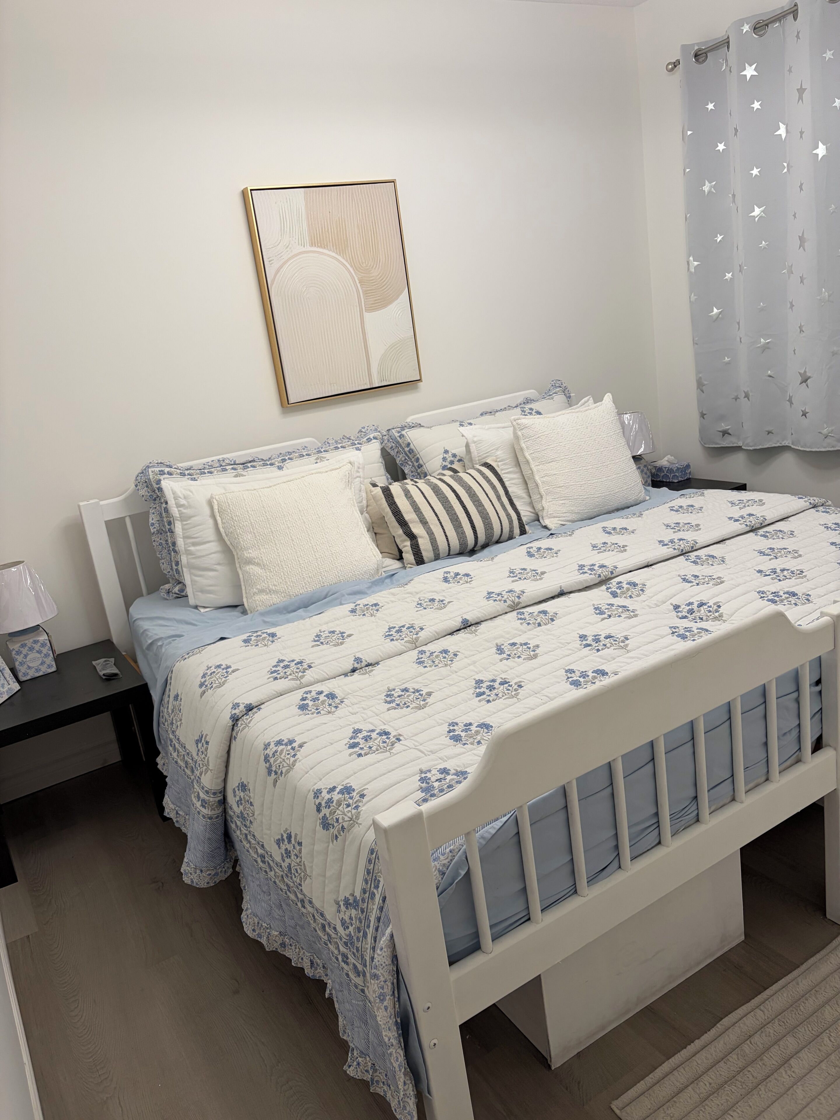 A bedroom with a white bed, a bedside table with a lamp, and a framed picture on the wall.