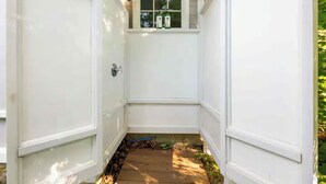A narrow outdoor pathway leading to a white door with a window above it, surrounded by greenery. - Oceanfront Escape: Beach Access on Private Estate (Gloucester)