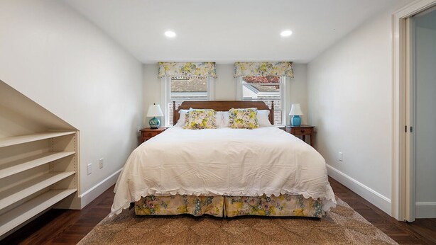 A bedroom with a large bed, two bedside tables, a window with floral curtains, and a door. - Oceanfront Escape: Beach Access on Private Estate (Gloucester)