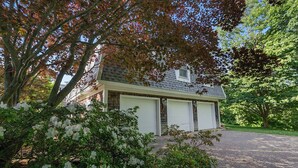 A two-story house with a garage, surrounded by trees and shrubs. - Oceanfront Escape: Beach Access on Private Estate (Gloucester)