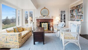 A living room with a fireplace, a sofa, a chair, and a bookshelf. - Oceanfront Escape: Beach Access on Private Estate (Gloucester)