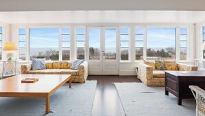 A spacious room with large windows, a wooden table, two sofas, and a dark wooden cabinet. - Oceanfront Escape: Beach Access on Private Estate (Gloucester)