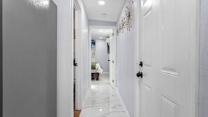 A hallway with white doors, a marble floor, and a bed in the distance.