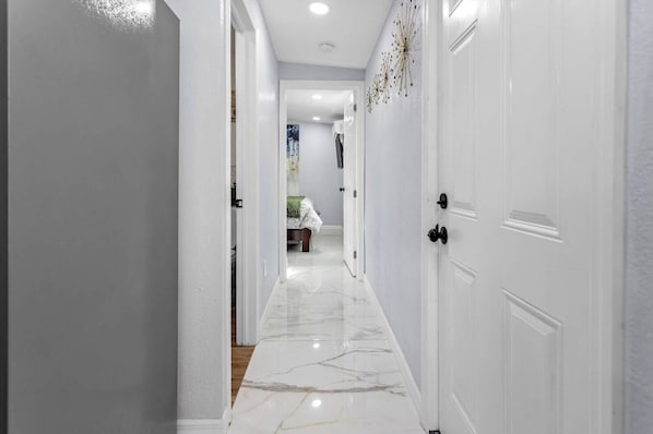 A hallway with white doors, a marble floor, and a bed in the distance.