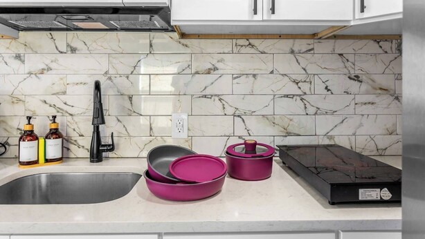 A kitchen with a marble backsplash, a stainless steel sink, and a black range hood.